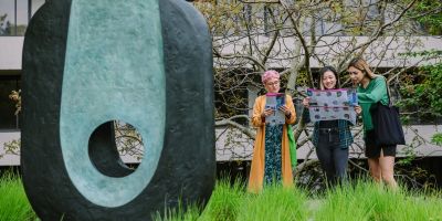 Three people stand looking at paper maps of the public art trail. A large abstract sculpture is in front of them.