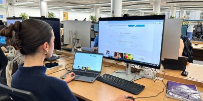 A student is sat at desk in the Brotherton West Building. Their laptop is to the left of them connected to a docking station. The student is looking ahead at a large monitor while using a keyboard and mouse.