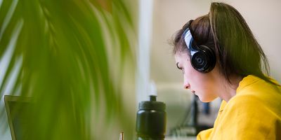 A student wears headphones while studying at a desk in the Library.