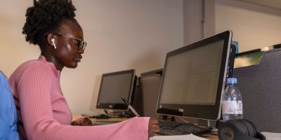 A student with earphones is holding a pen while reading text from a screen.
