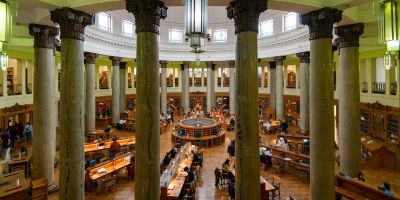 A view looking over a round library reading room with green stone columns and a hanging chandelier.