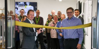 Professors Jeffrey Grabill and Nick Plant are cutting a gold ribbon on the doors of the Library Makerspace. Behind them is a group of smiling people also at the Library Makerspace launch.