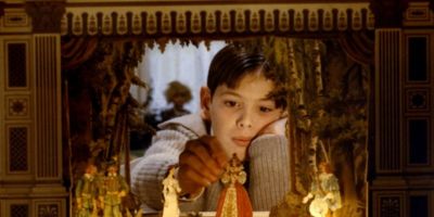 A young child is playing with a toy stage. The child is holding a character in one hand and resting their head with their other hand. In front of the stage are several candles stood in a row.