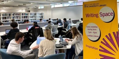 Students working on laptops and reading at shared tables in a modern library space. A large yellow banner in the foreground reads 