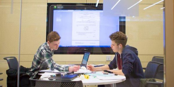 Students occupying a group room seated in front of a large computer screen