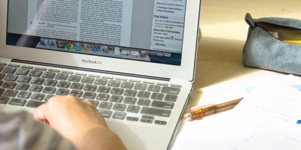 A close up view of someone working at a desk on a laptop  computer