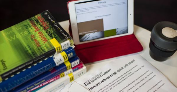 Desk with referencing guide visible on iPad and Leeds Harvard crib sheet print out